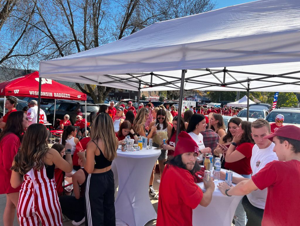 Packed fan zone of Badgers fans around cocktail tables under GameDay Your Way tents on Regent Street.