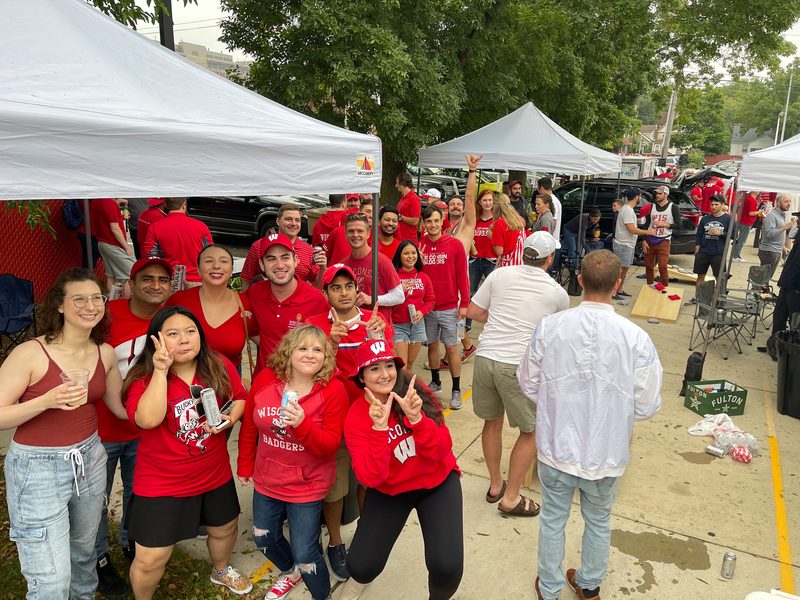 Wisconsin Badgers fans celebrating together at a GameDay Your Way tailgate with white tents in Madison.
