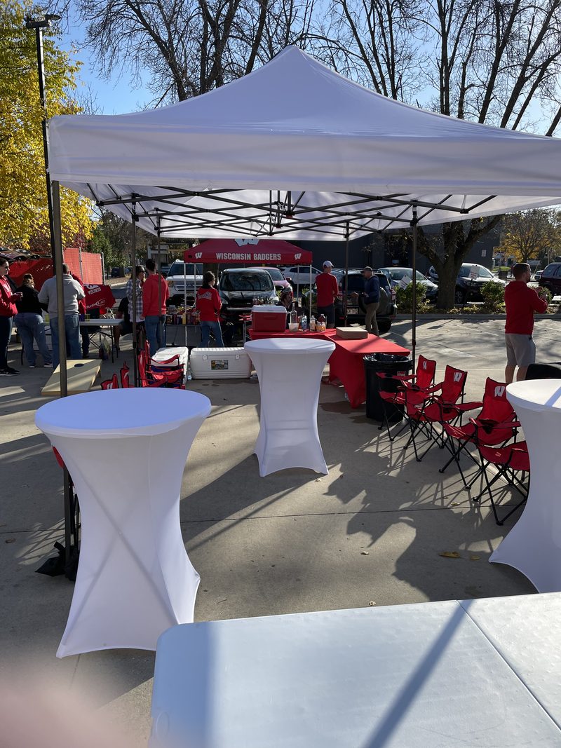 Private cabana setup with a Wisconsin Badgers tent, white cocktail tables and red chairs at a GameDay Your Way Regent Street tailgate in Madison.