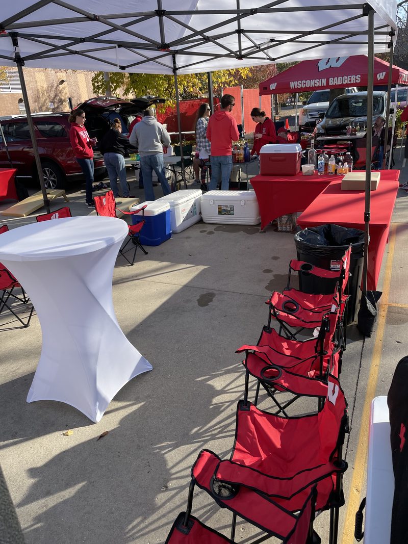 Wisconsin Badgers tailgate setup with coolers and seating under a GameDay Your Way tent in Madison.