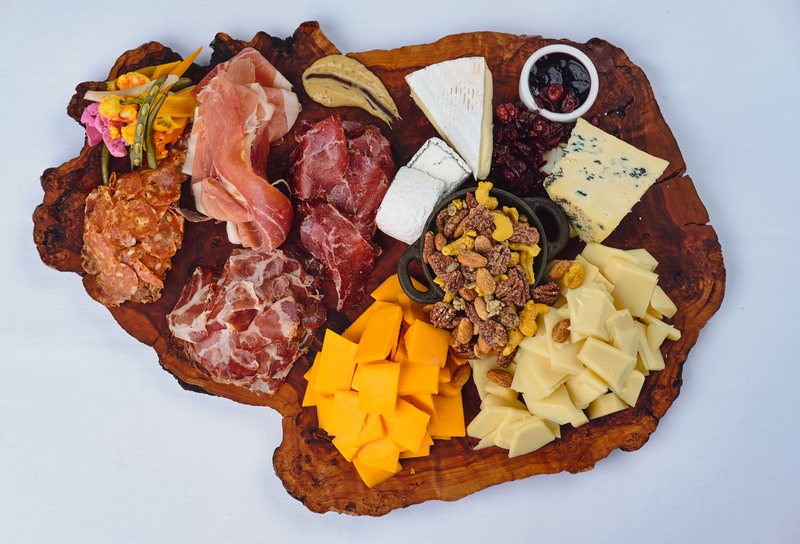 Heritage Catering charcuterie and cheese board — prosciutto, coppa and salami with Wisconsin cheddar, brie and blue, candied nuts and preserves on a live-edge wooden board.